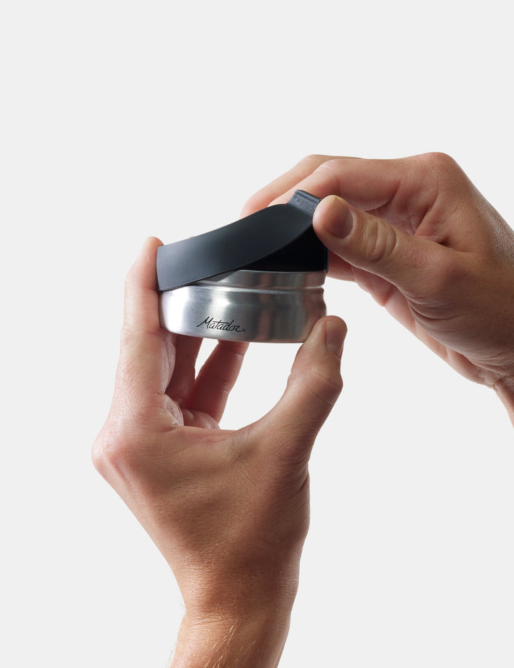 Matador Waterproof Travel Canister - 100ml - person holding a metallic container with a black lid on a light gray background