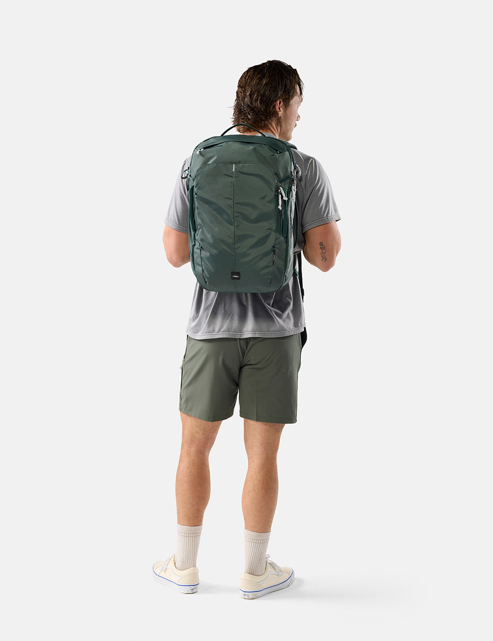 Matador 30L Carry-On Travel Pack in Juniper - person wearing a green backpack and shorts on a white background