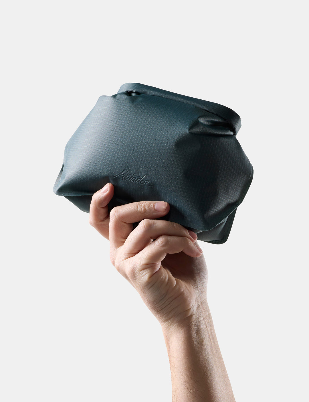Matador FlatPak Waterproof Toiletry Case (V2) in Juniper - hand holding a Blue-green toiletry bag against a light gray background