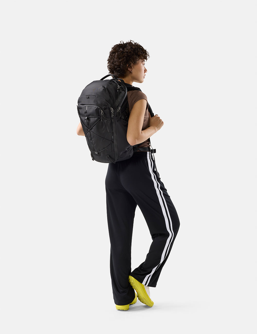Matador 24L Adventure Pack in Black - person wearing a black backpack and black pants with white stripes on a white background