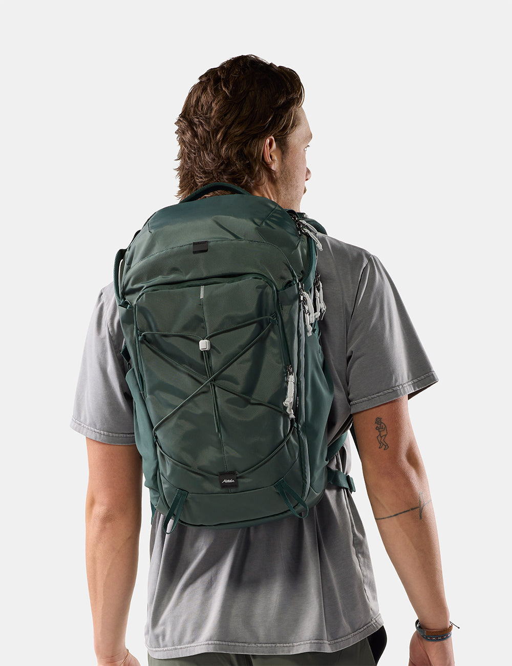 Matador 24L Adventure Pack in Juniper - a man wearing a dark green technical backpack, viewed from behind to show the fit and design, against a light gray studio background