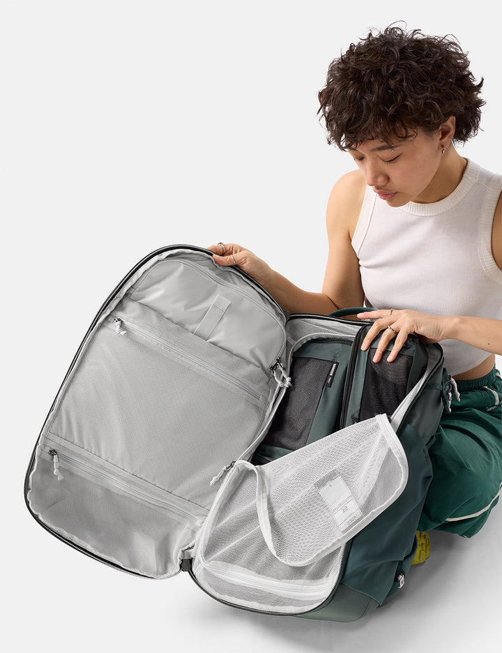 Matador 35L Global Travel Pack in Juniper - person organizing a green backpack with multiple compartments on a white background
