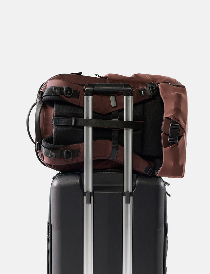 Matador 35L Global Travel Pack in Garnet - garnet backpack on top of a black suitcase with silver handle on a light gray background