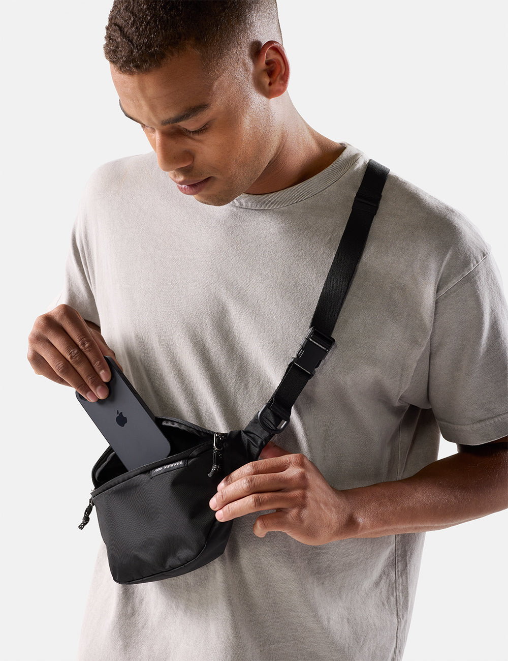 Matador 2L Lite Sling in Black - man wearing a black waist bag with iphone on a light gray background