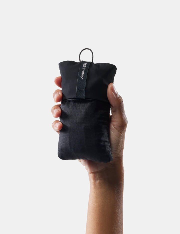 Matador Blackout Eyemask + Earplugs Kit - hand holding a black compression sack with a brand logo on a white background