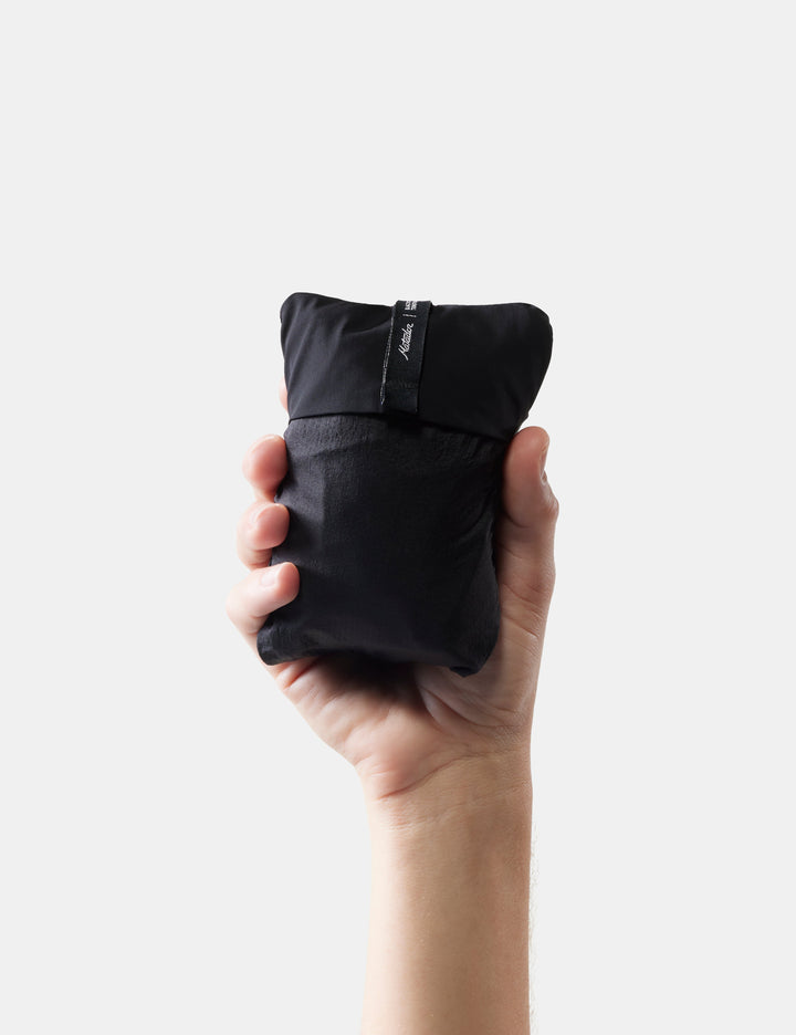 Matador Blackout Travel Pillow - hand holding a packed black travel pillow against a white background