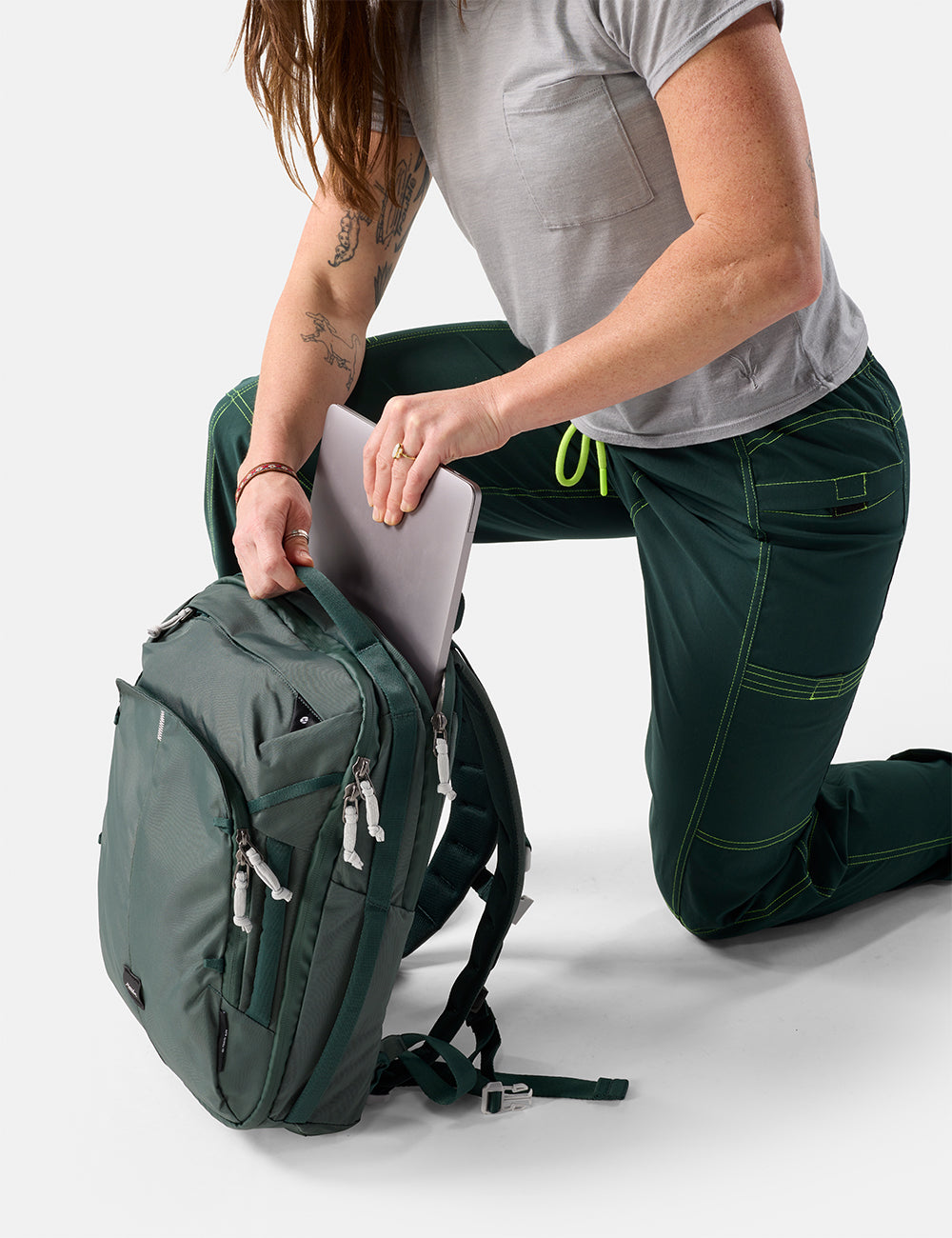 Matador 18L Personal Item Travel Pack in Juniper - person kneeling on a white surface with a green backpack and gray shirt
