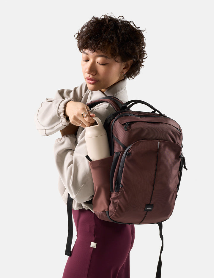 Matador 18L Personal Item Travel Pack in Garnet - person pulling water bottle out of garnet backpack