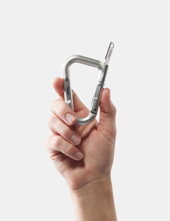 Matador BetaLock in Matte Black - hand holding a silver carabiner against a white background