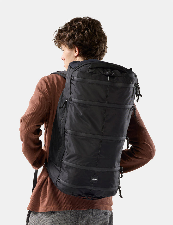 Matador 45L SEG Hybrid Travel Pack in Black - a man wearing a large black backpack, photographed from behind against a light gray studio background
