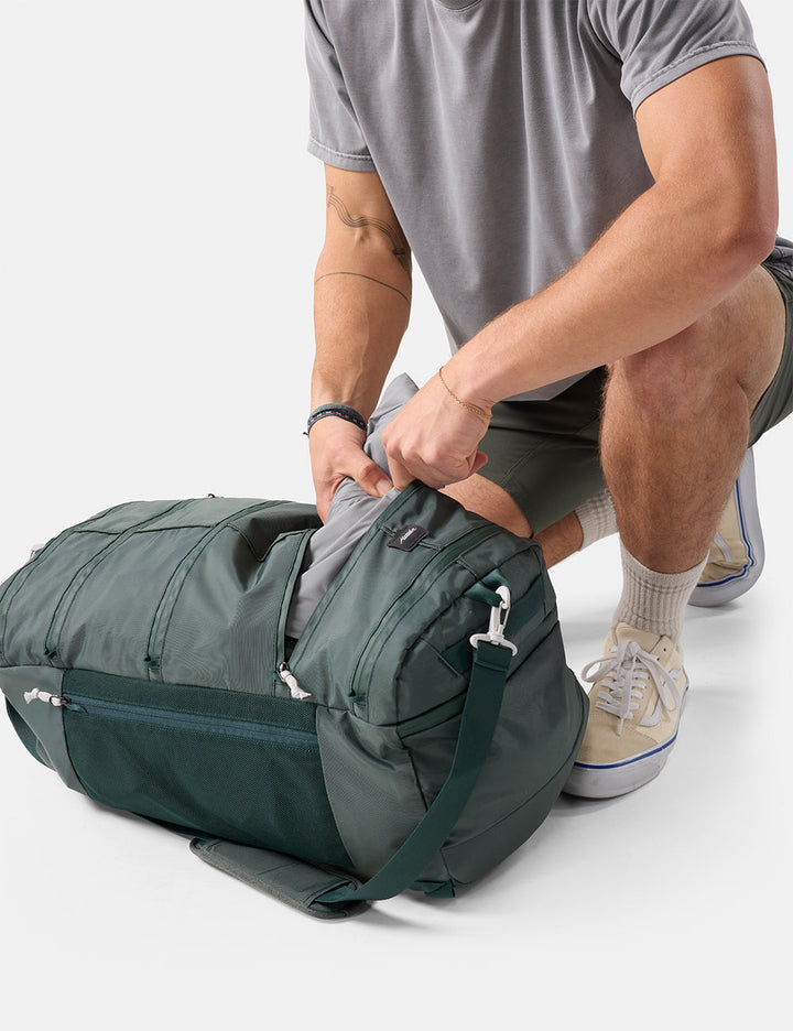 Matador 45L SEG Hybrid Travel Pack in Juniper - person packing a green duffel bag on a white background