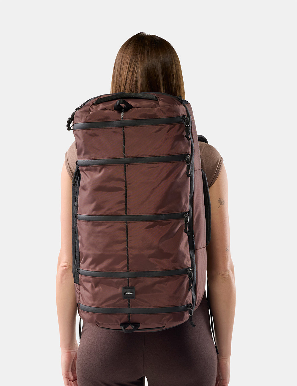 Matador 45L SEG Hybrid Travel Pack in Garnet - a woman viewed from behind wearing a large garnet segmented backpack against a light gray studio background