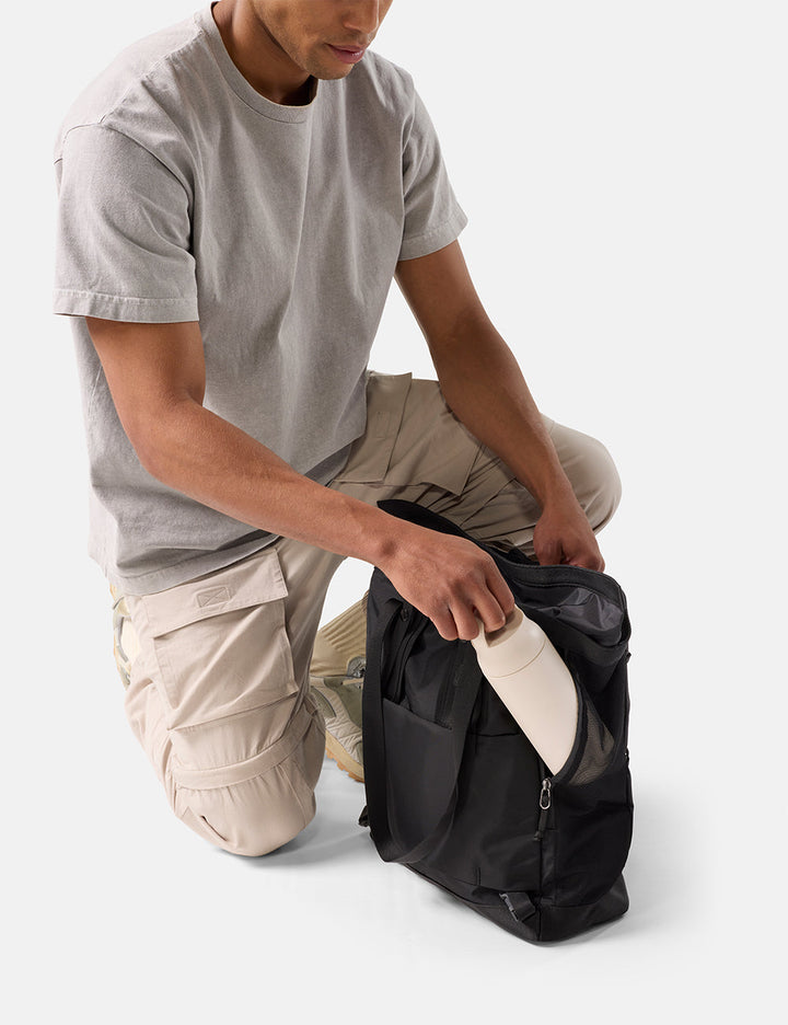Matador 24L Tote Pack in Black - person placing water bottle in black tote pack on a white background