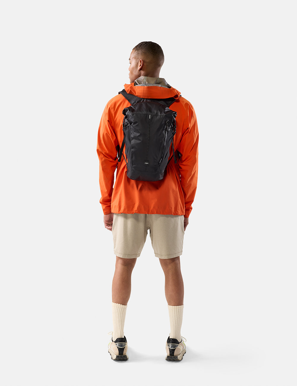 Matador 18L Waterproof Packable Backpack in Black - person wearing an orange jacket and black backpack on a white background
